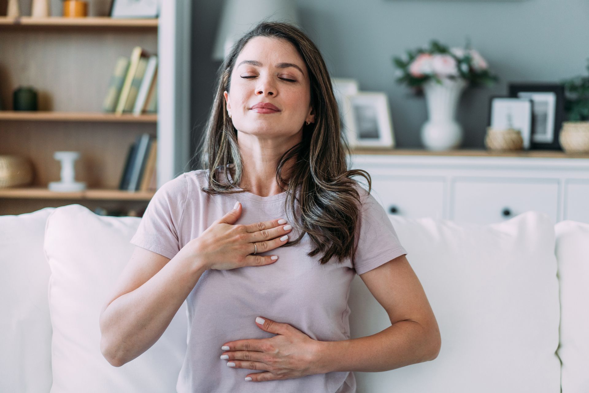 A woman is sitting on a couch with her eyes closed and her hands on her chest.
