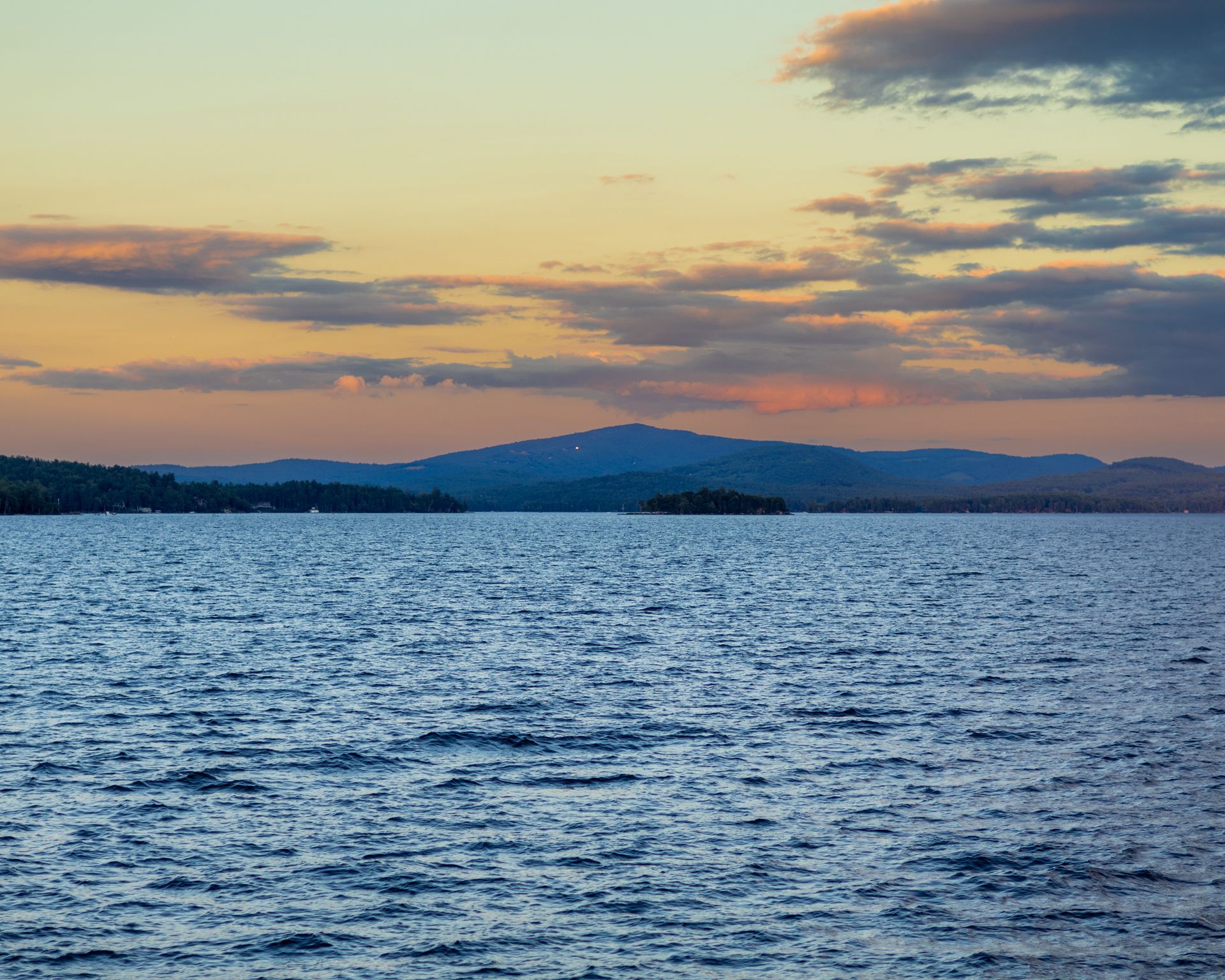 A rippling lake under a colorful sunset sky with rolling mountains in the background.