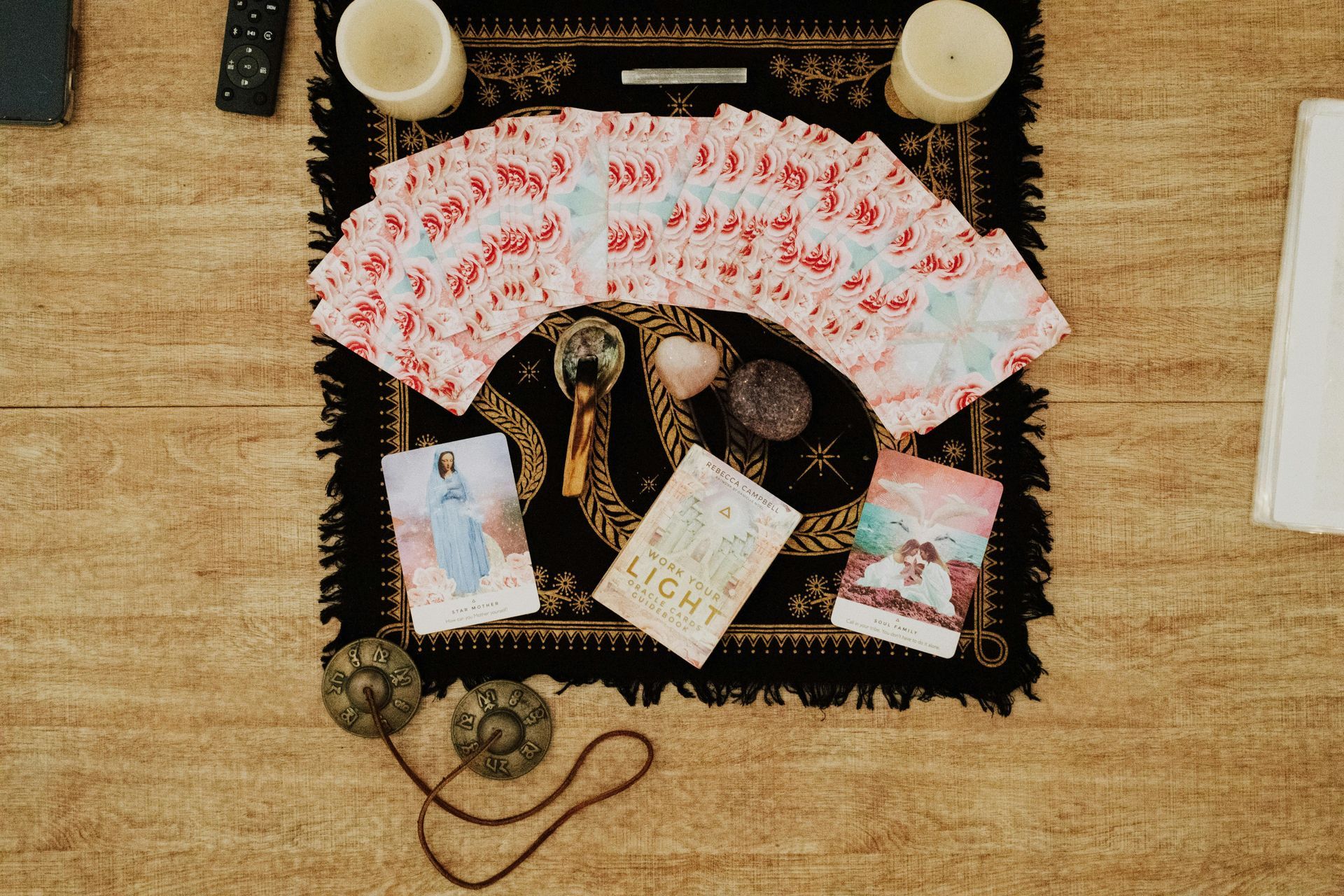 A tarot card spread arranged on a black mat with candles, crystals, and small cymbals on a wooden surface.