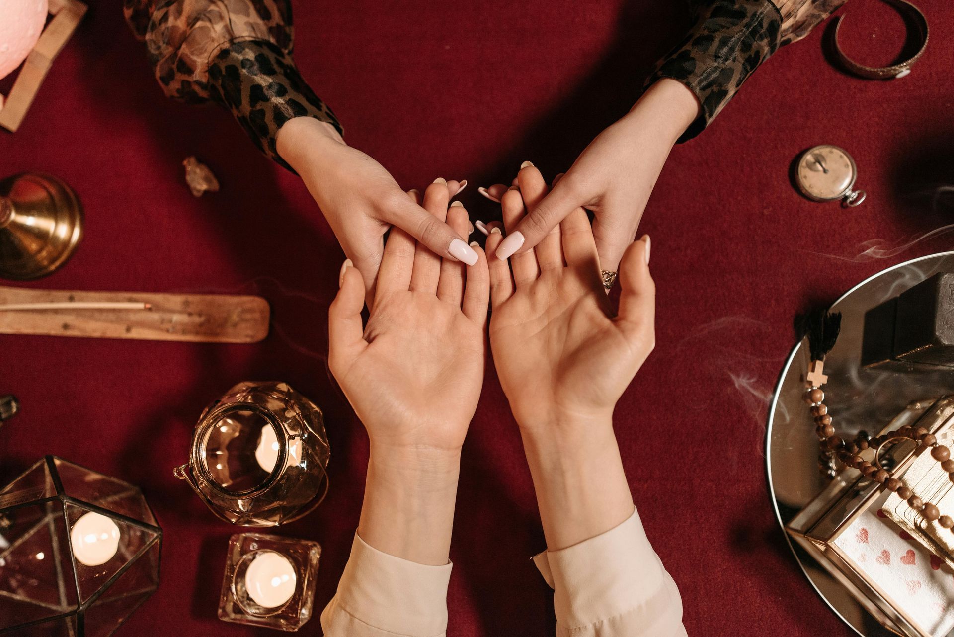 Hands during palm reading on a red tablecloth with candles, crystals, and other fortune-telling items.