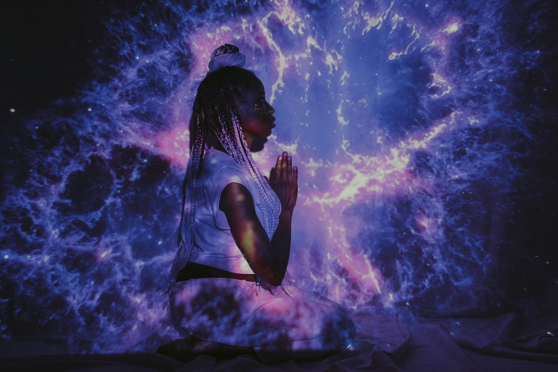 A woman is praying in front of a projection of a galaxy.