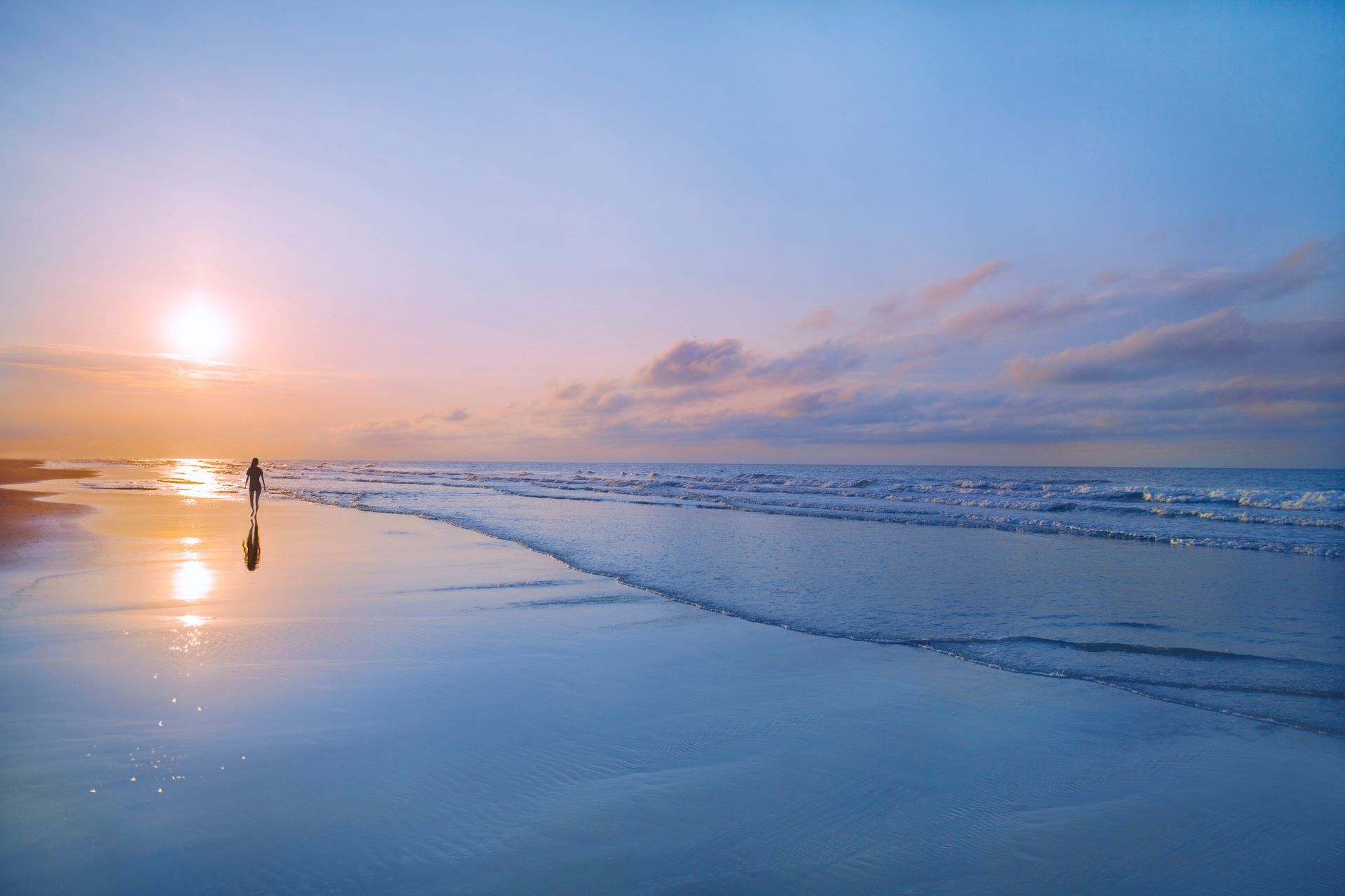 A person is standing on a beach at sunset.