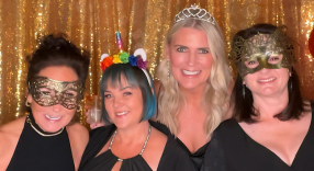 Four women wearing masks and tiaras are posing for a birthday picture