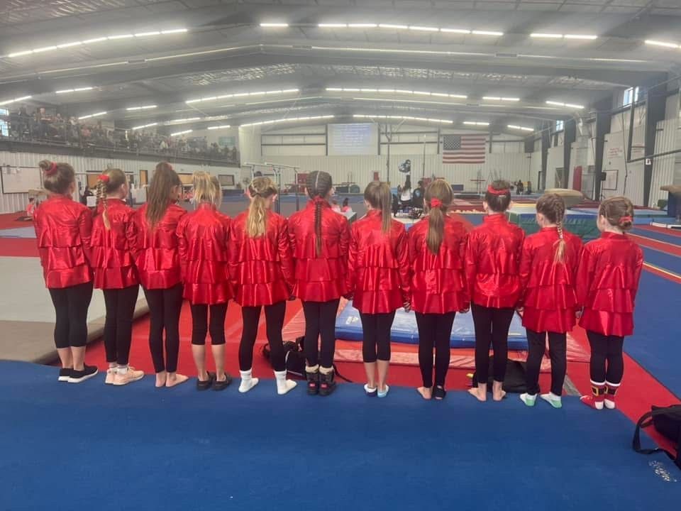 A group of young girls in red jackets are standing in a gym