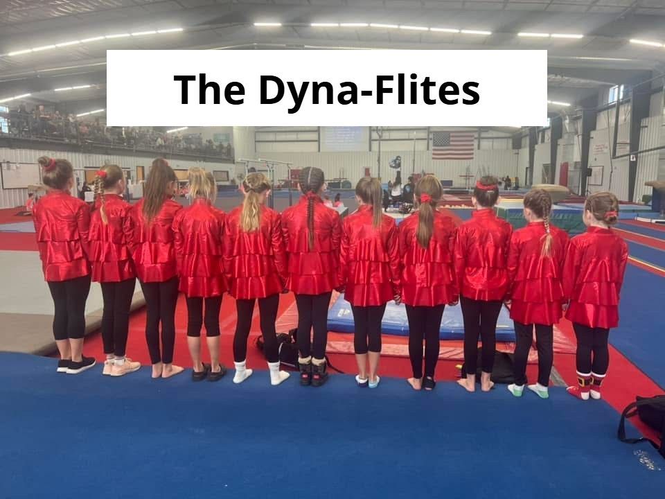 A group of young girls in red jackets are standing in a gym under a sign that says the dyna-flites