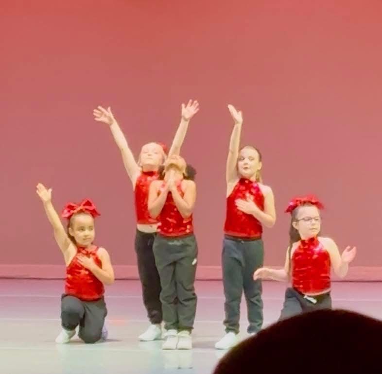 A group of young girls are dancing on a stage with their arms in the air