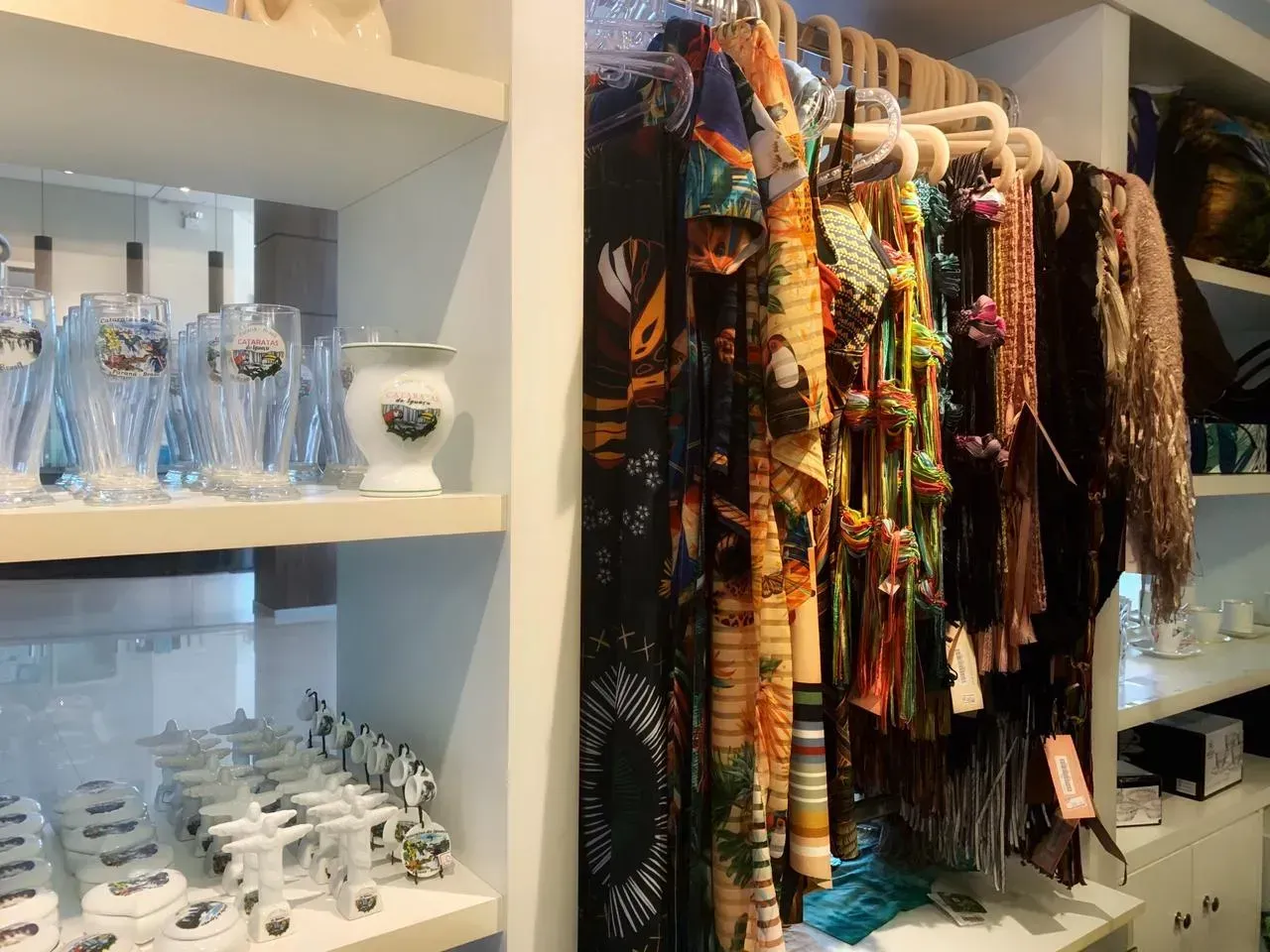 Prateleiras com mercadorias em uma loja, incluindo artigos de vidro, cachecóis e itens decorativos.