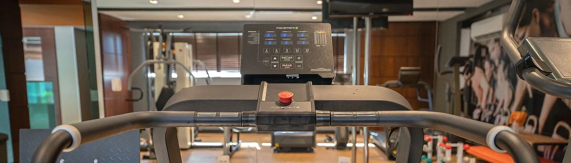 Interior de academia com uma esteira em foco e outros equipamentos visíveis ao fundo.