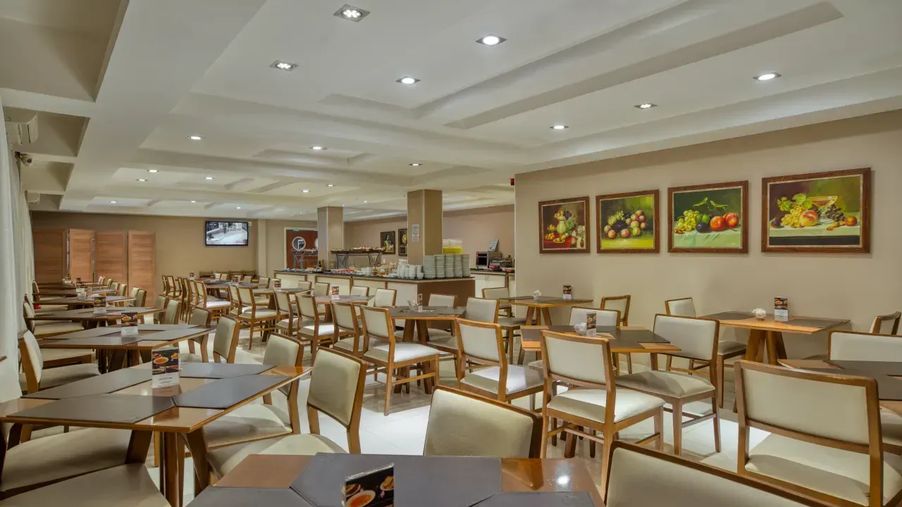 Interior do restaurante com mesas, cadeiras e pinturas de natureza morta emolduradas.