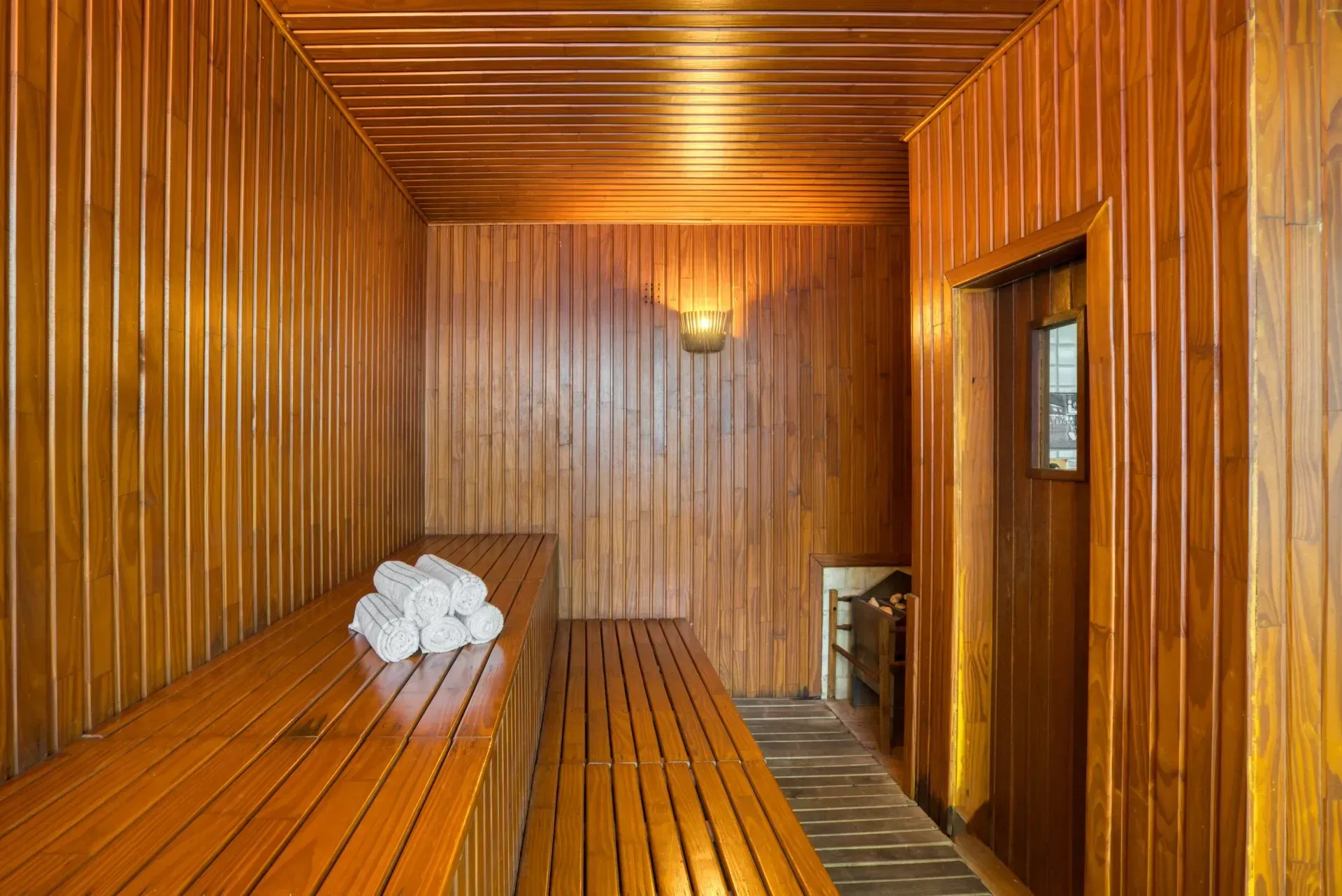Interior de sauna de madeira com bancos, toalhas e porta.