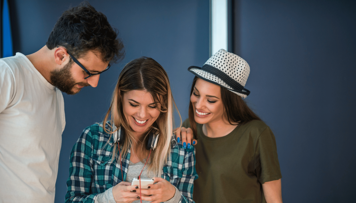 A man and two women are looking at a cell phone together.