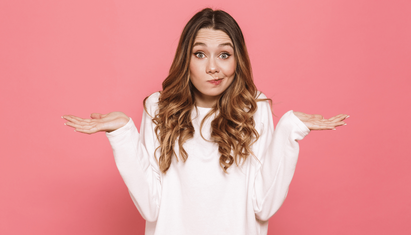 A woman in a white sweater is shrugging her shoulders on a pink background.