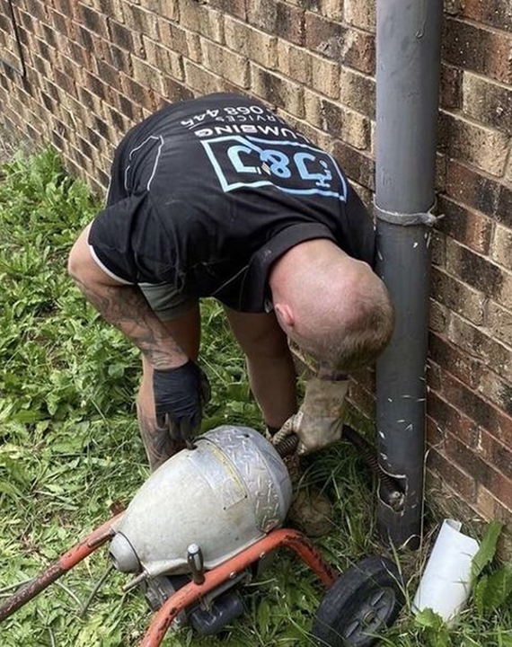 A man is kneeling down next to a drain pipe.