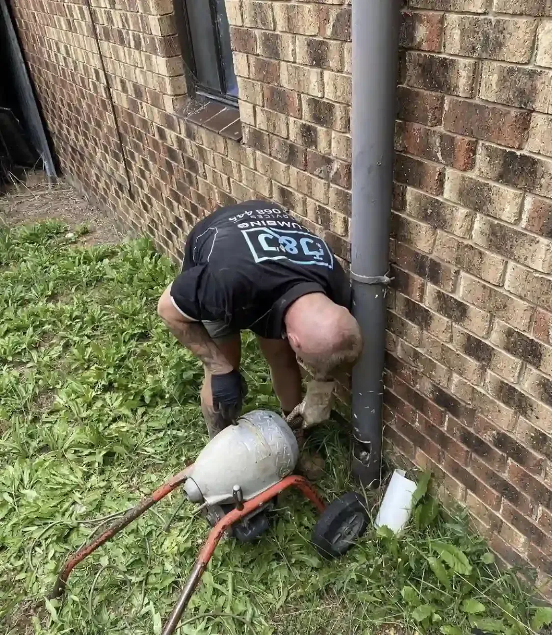 A man is kneeling down next to a drain pipe.