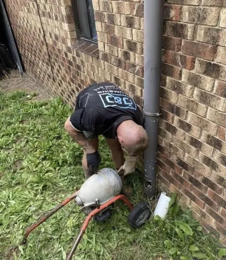 A man is kneeling down next to a drain pipe.