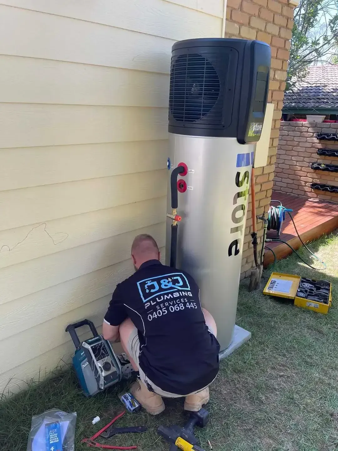 A man is working on a water heater outside of a house.
