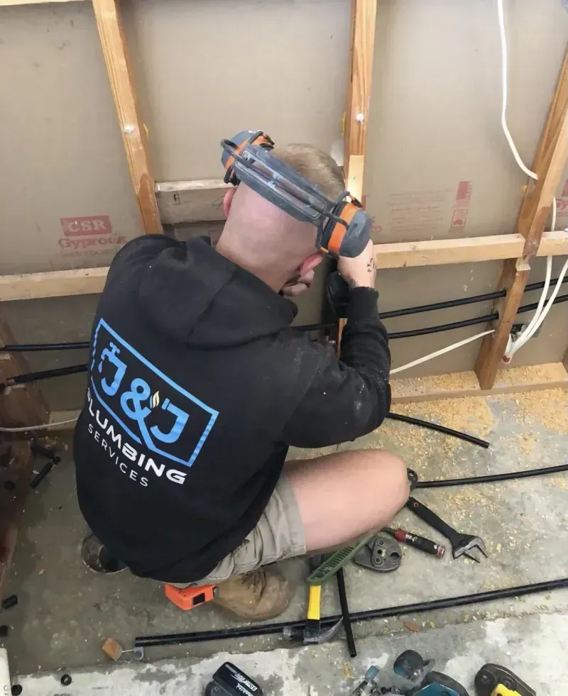 A man wearing a j & j plumbing hoodie is working on a wall.