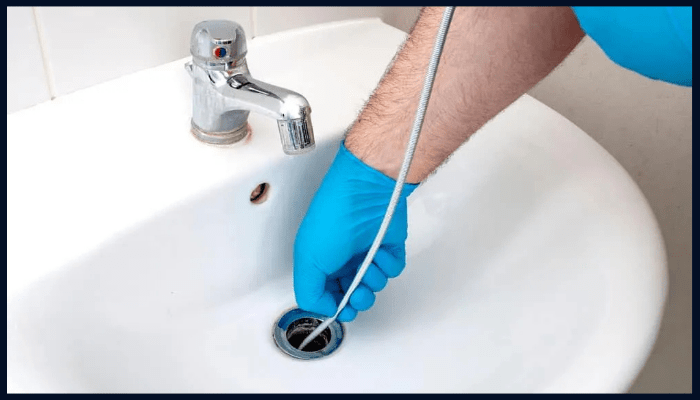 Plumber using a drain snake to clear a partially blocked bathroom sink, showing early warning signs of drain problems.