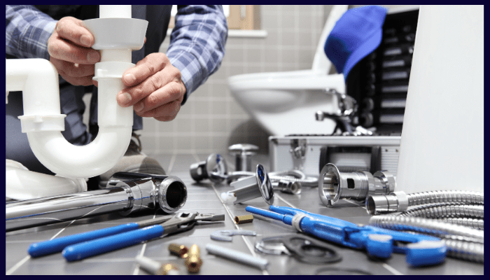 Plumber assembling a white plastic P-trap in a bathroom, surrounded by tools.
