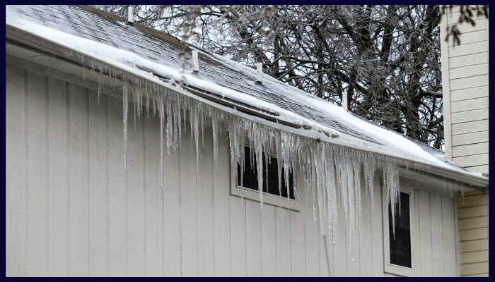 heavy icicles and frozen gutters along a roof edge in winter