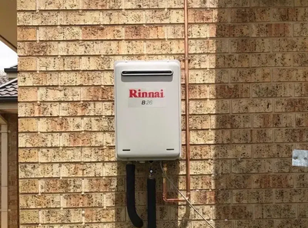 A white rinnai water heater is mounted on a brick wall.