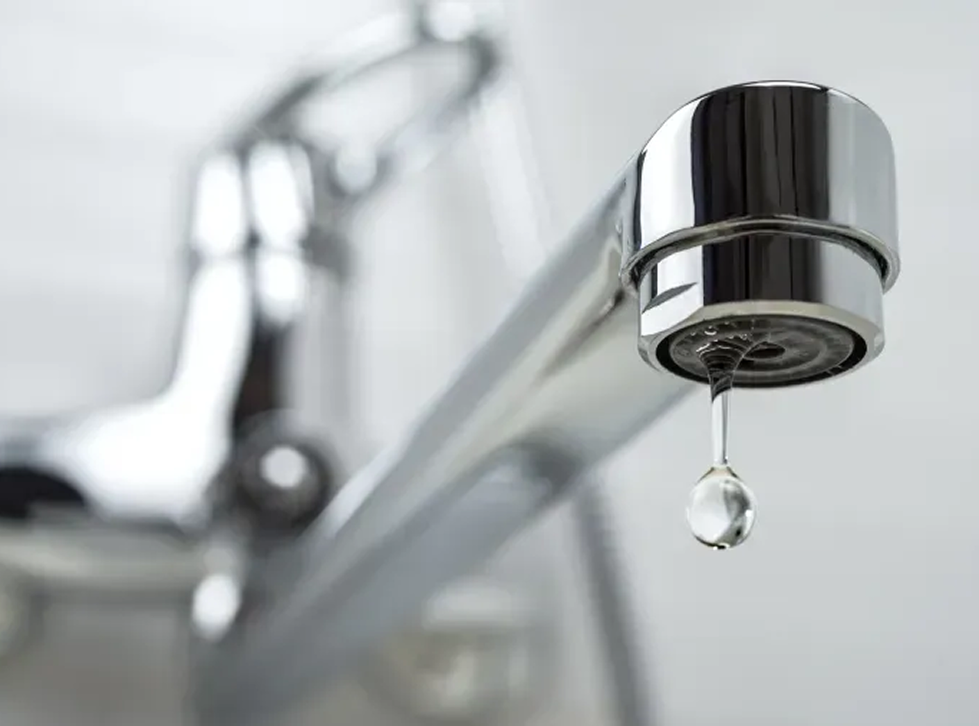 A close up of a faucet with a drop of water coming out of it.