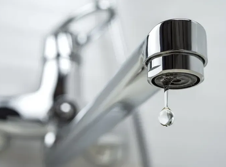 A close up of a faucet with a drop of water coming out of it.