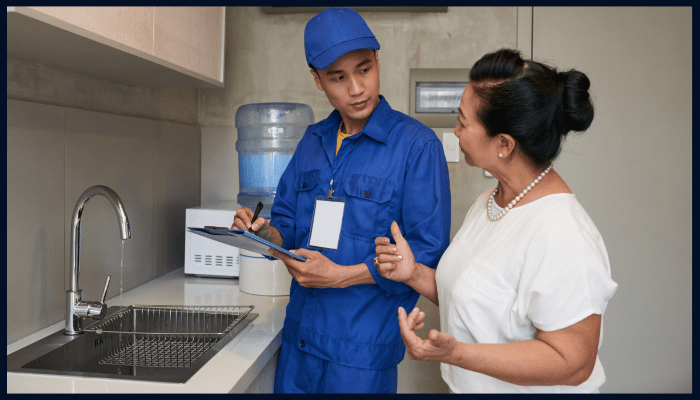 Professional plumber discussing plumbing maintenance checklist with Canberra homeowner in kitchen.