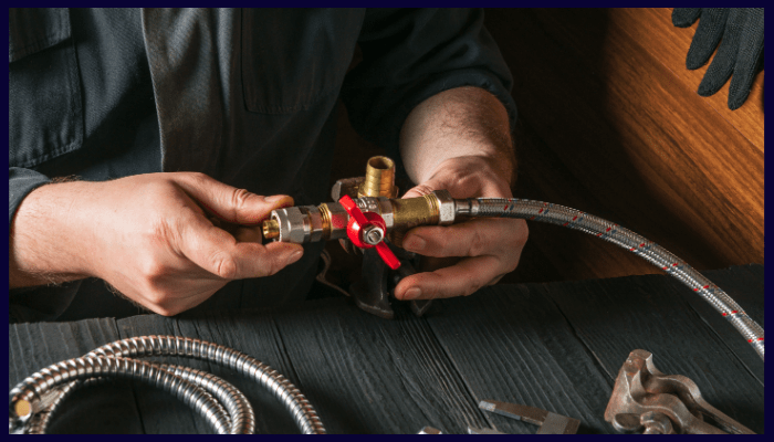 Plumber connecting a hose to a valve, using tools.