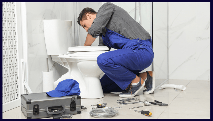 A plumber is fixing a toilet in a bathroom.