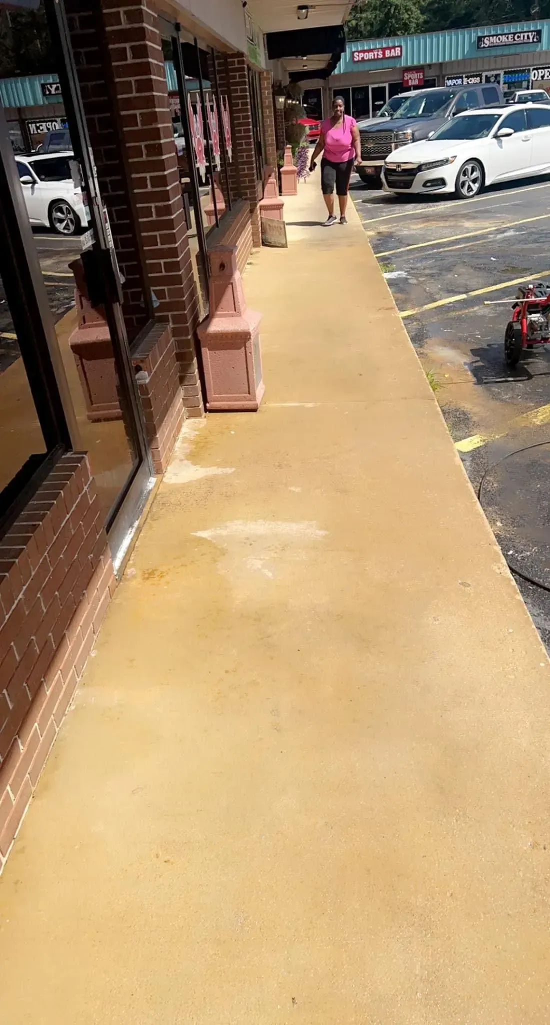 A woman is walking down a sidewalk next to a parking lot.