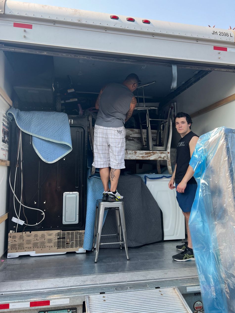 Two men loading furniture into a moving truck. One stands on a stool; the other watches.