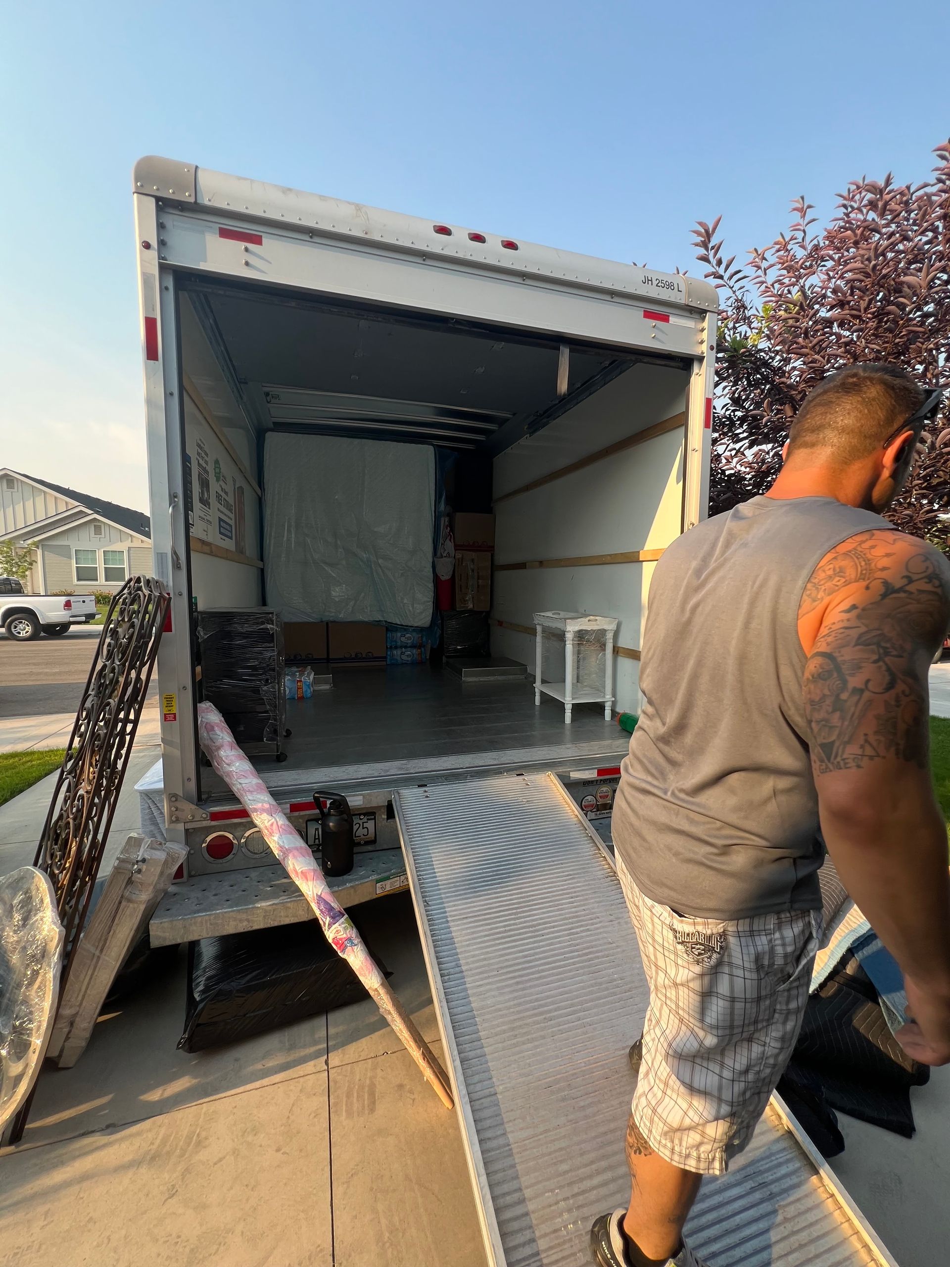 A person loads a moving truck parked in a driveway; the truck's ramp is extended.