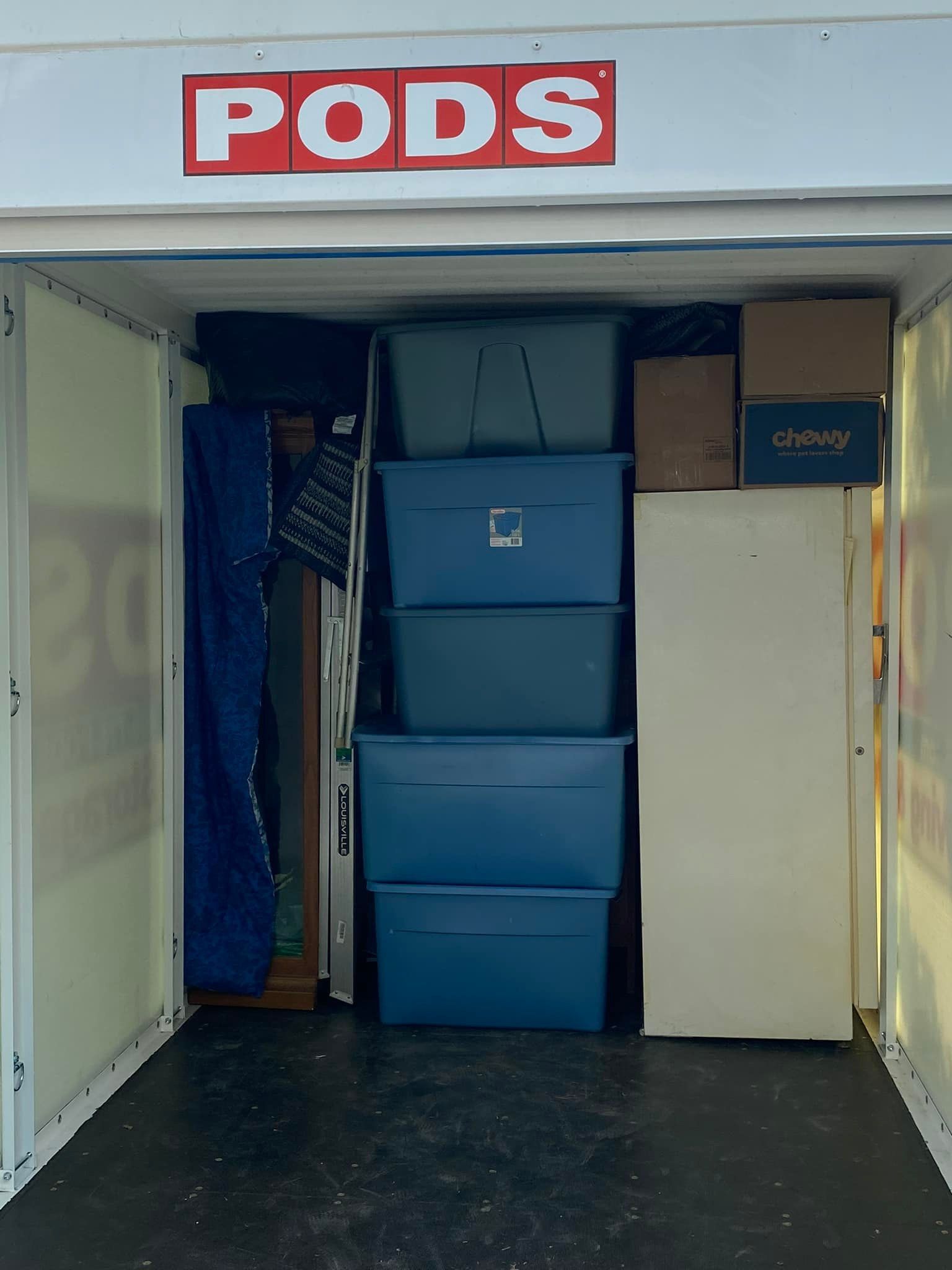 Inside a PODS storage unit, packed with blue bins, boxes, and furniture wrapped in blue pads.