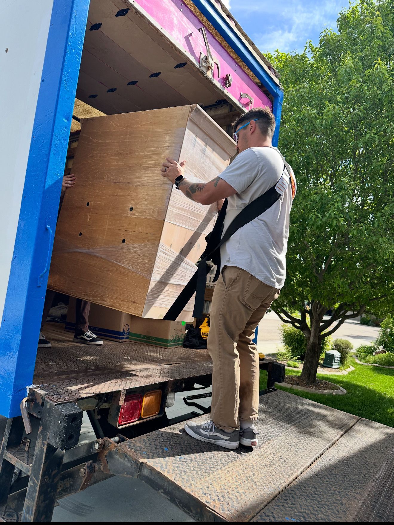 Two movers loading a large wooden cabinet into a truck. One is in tan pants and a grey shirt.