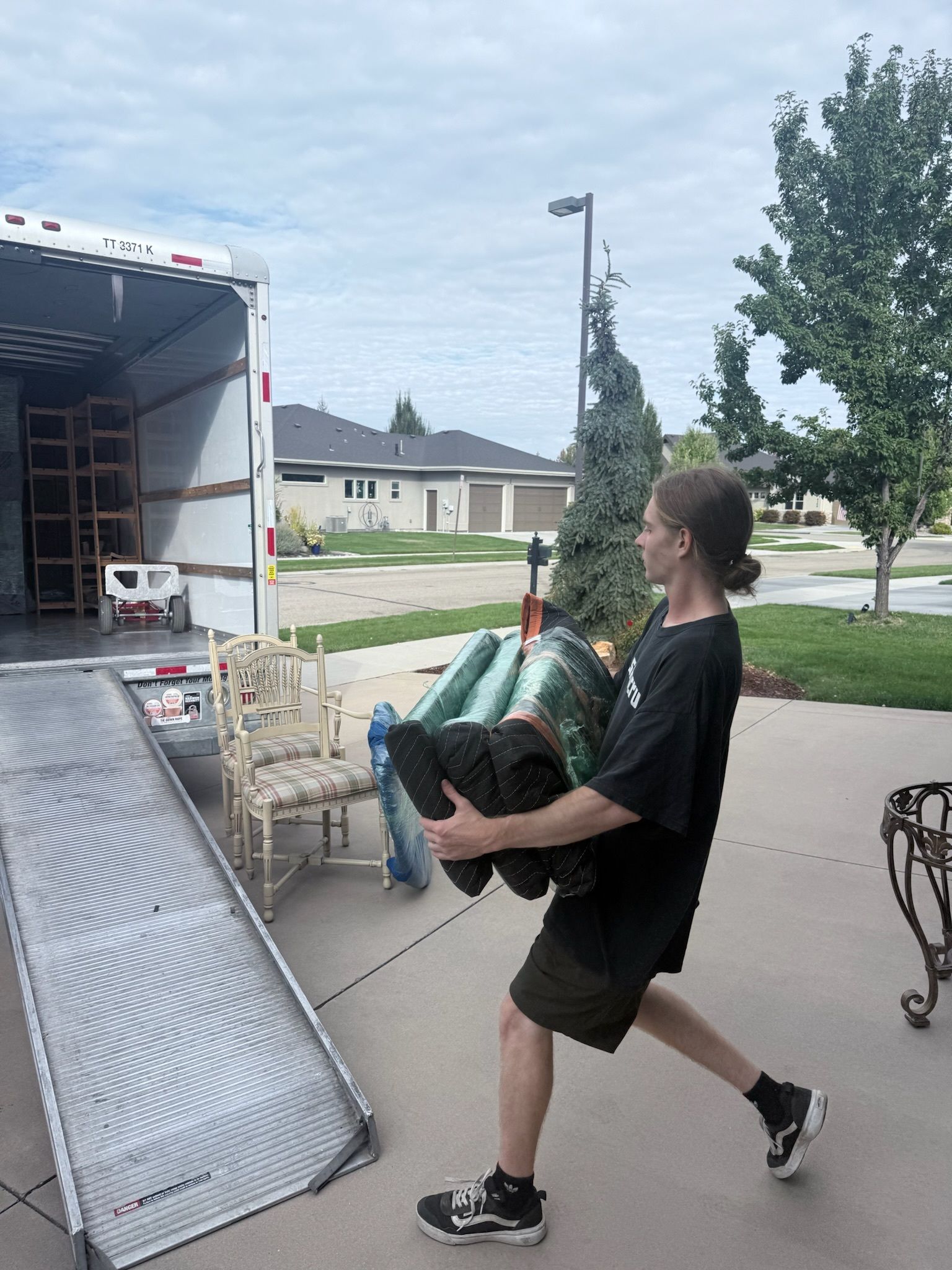 A living room with a gray couch, cardboard boxes, a rolled rug, and a palm plant; preparing to move.