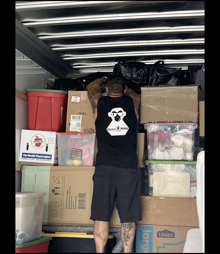 Man loading boxes into a moving truck; wearing a black tank top and shorts.