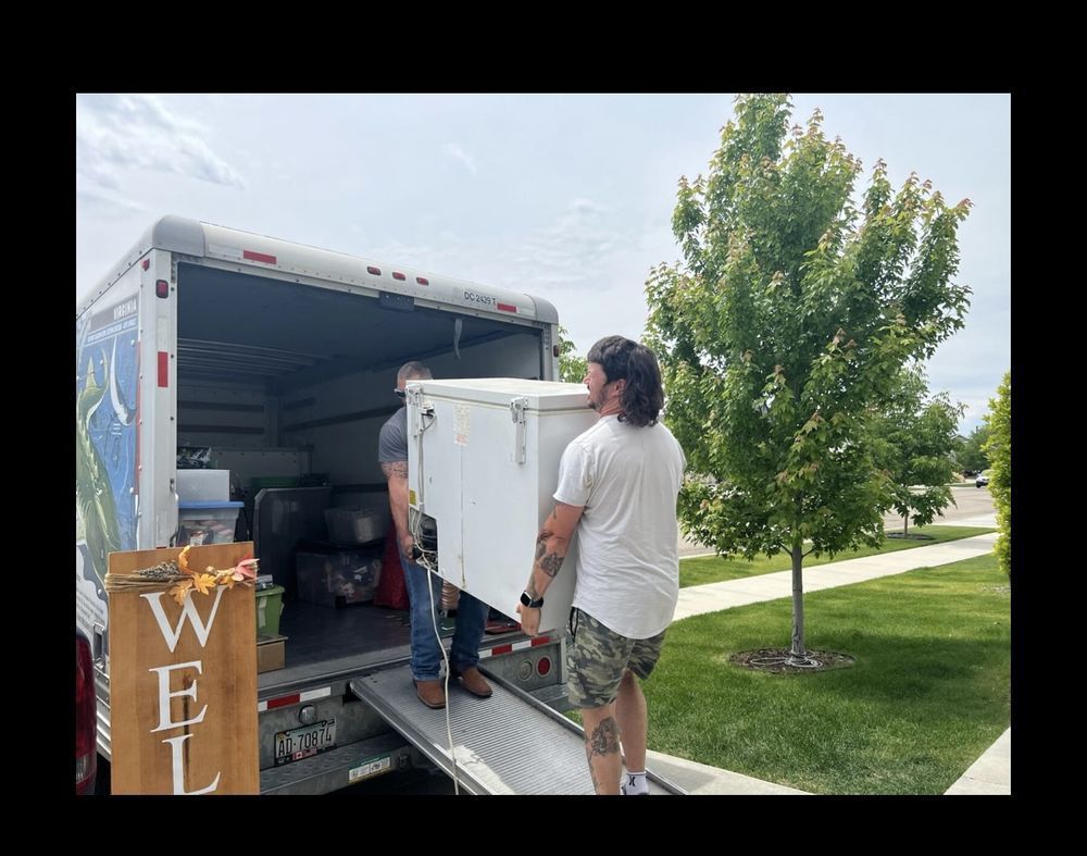 Two people loading a white box into a moving truck, outdoors.