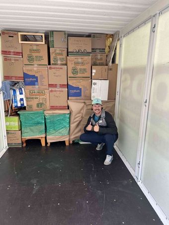 Man in a storage container, surrounded by packed boxes. He gives thumbs-up.