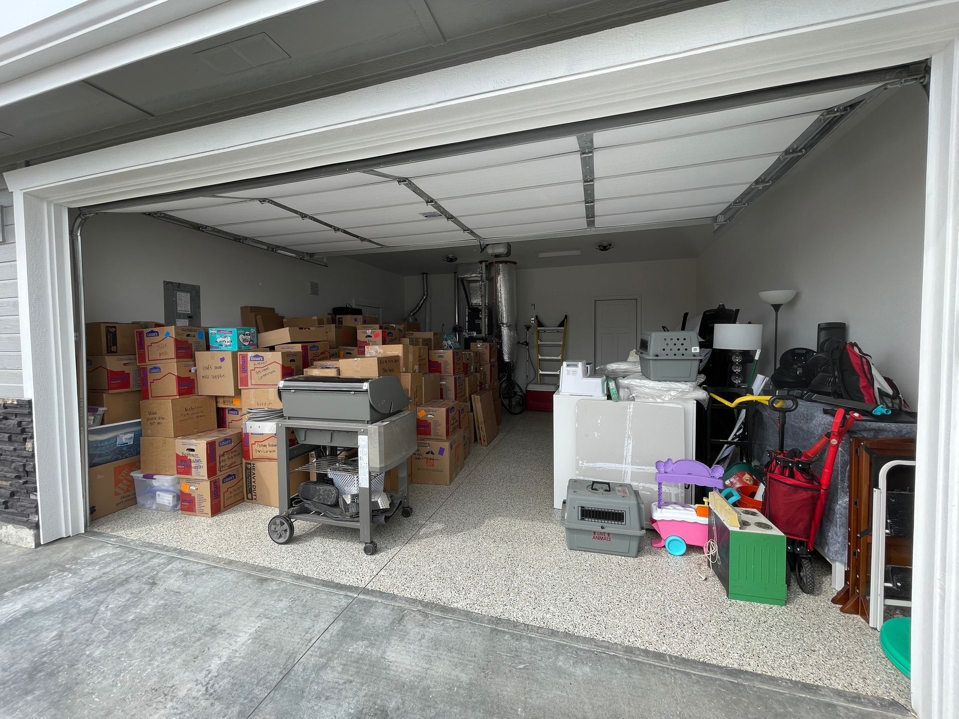 Garage interior filled with boxes, appliances, and various items. The garage door is open.