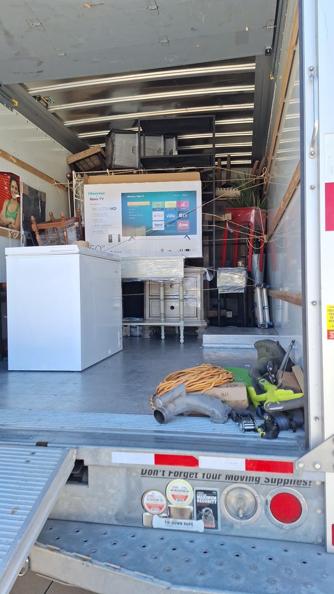 Inside of a moving truck with various household items, including a fridge, large TV, and appliances.