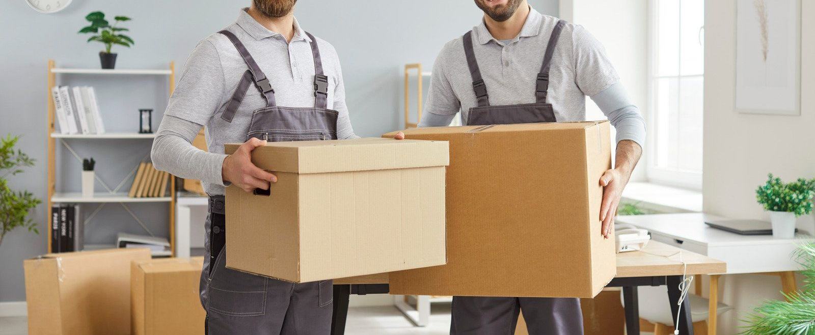 Two movers carrying cardboard boxes in a room, preparing to move.