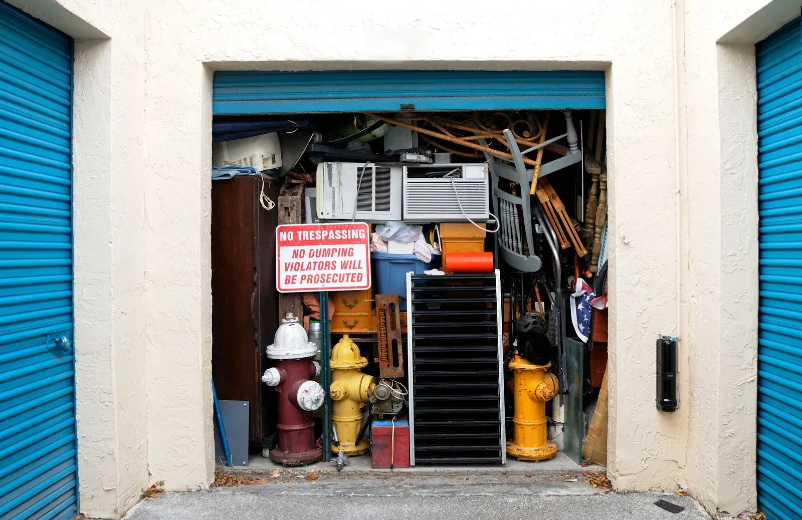 A storage unit overflowing with miscellaneous items: air conditioner, hydrants, chairs, boxes, and more.