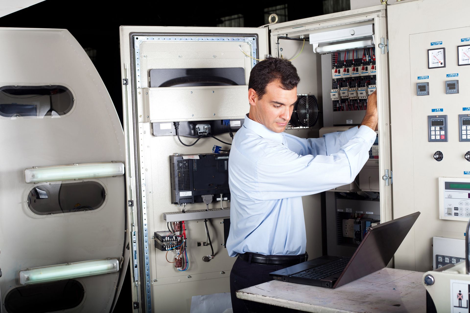 A man at a laptop attending to some electrical components in a box