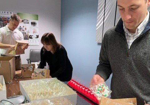 Three Seifert employees around a table, placing cookies in cardboard boxes