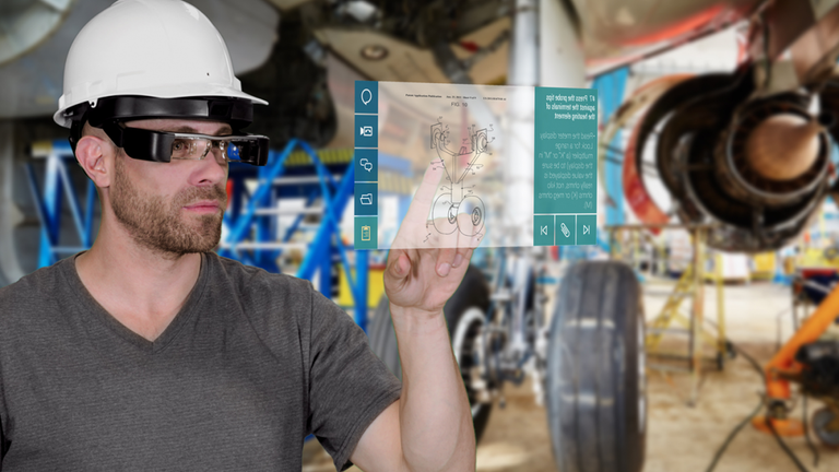 A man in a hard hat in a warehouse with AR glasses. He is pointing at a popup display.