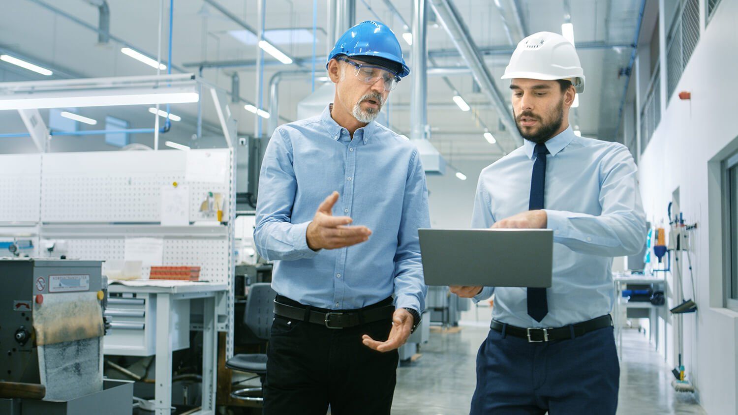 Two people with hard hats at a research facility looking at a laptop
