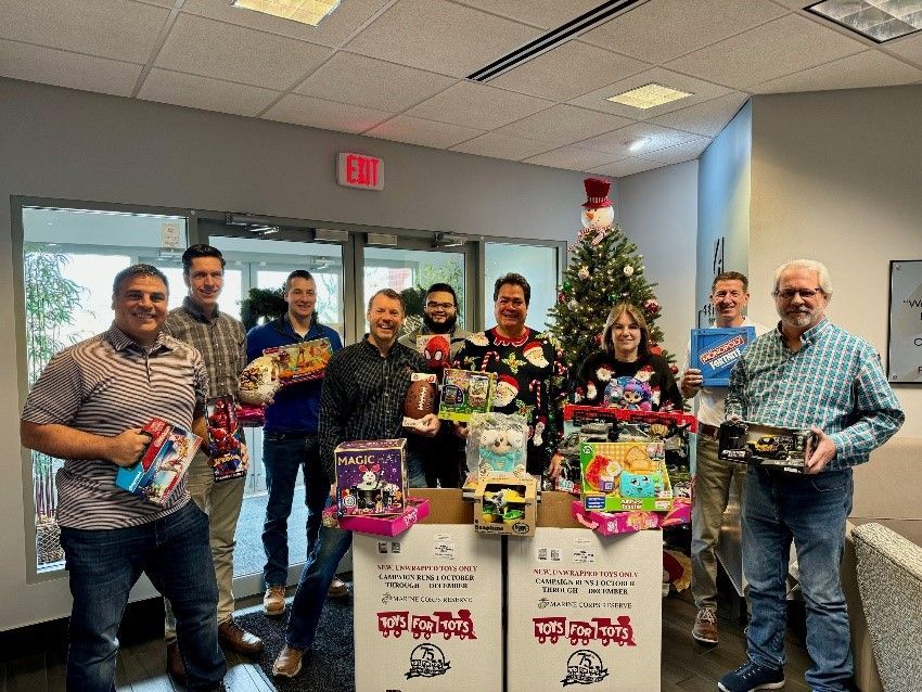 Seifert employees holding new toys, next to two Toys for Tots boxes. 