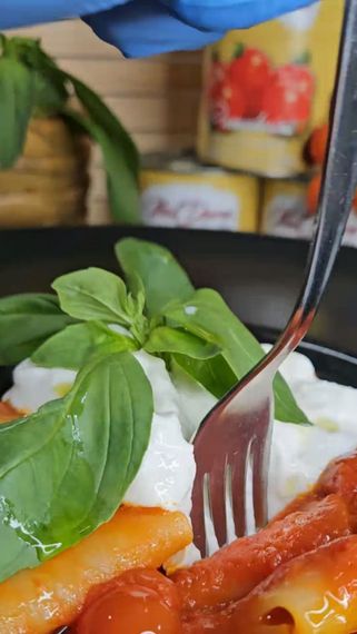 Servite la pasta condita con basilico, salsa bianca cremosa e pezzetti di pomodoro su un piatto nero.