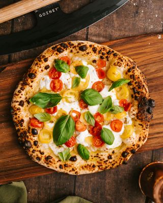 Pizza Margherita con basilico e pomodorini su un tavolo di legno.